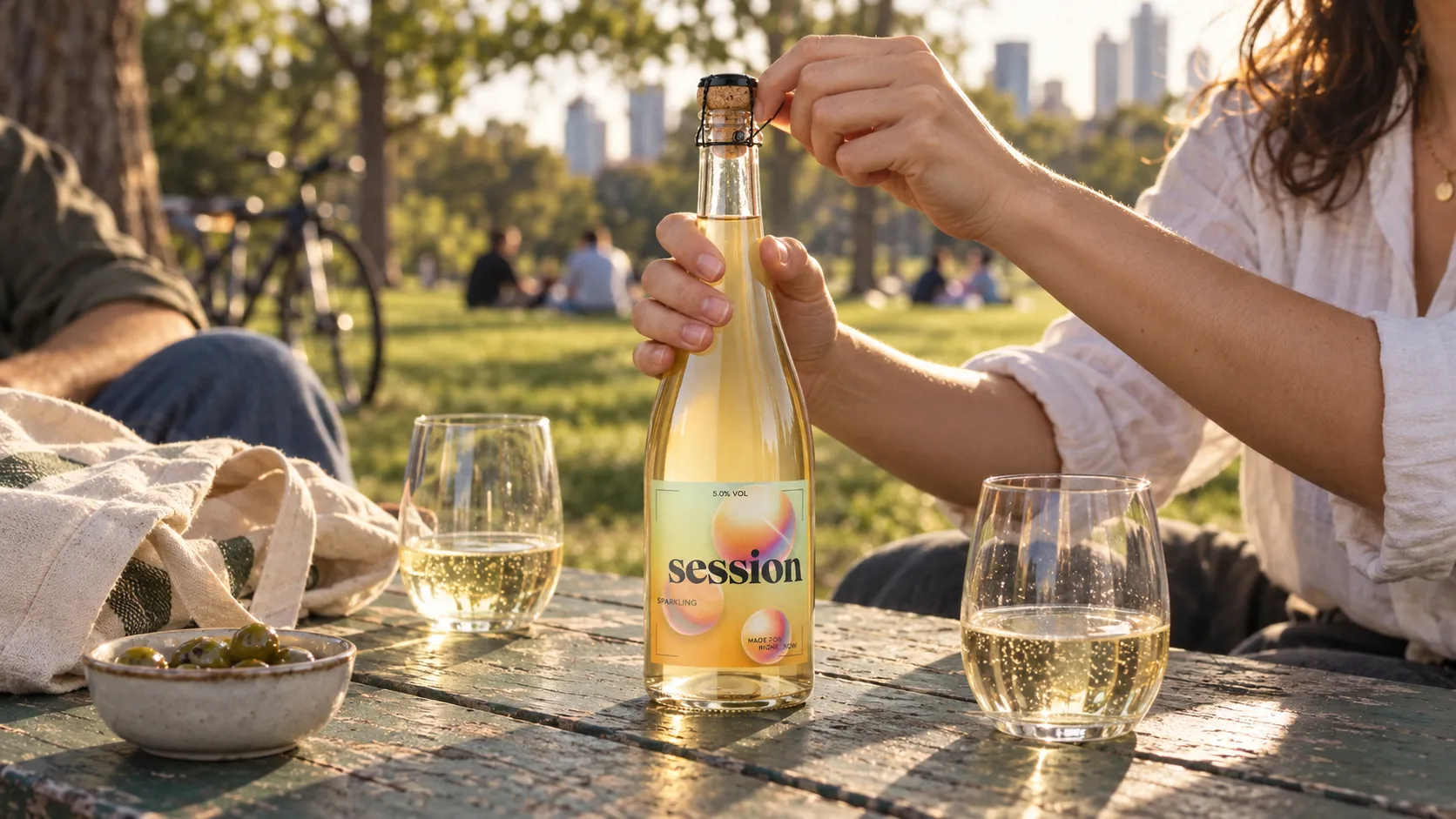 Complete SESSION WINE Sparkling bottle being opened on a worn park table in early-evening light