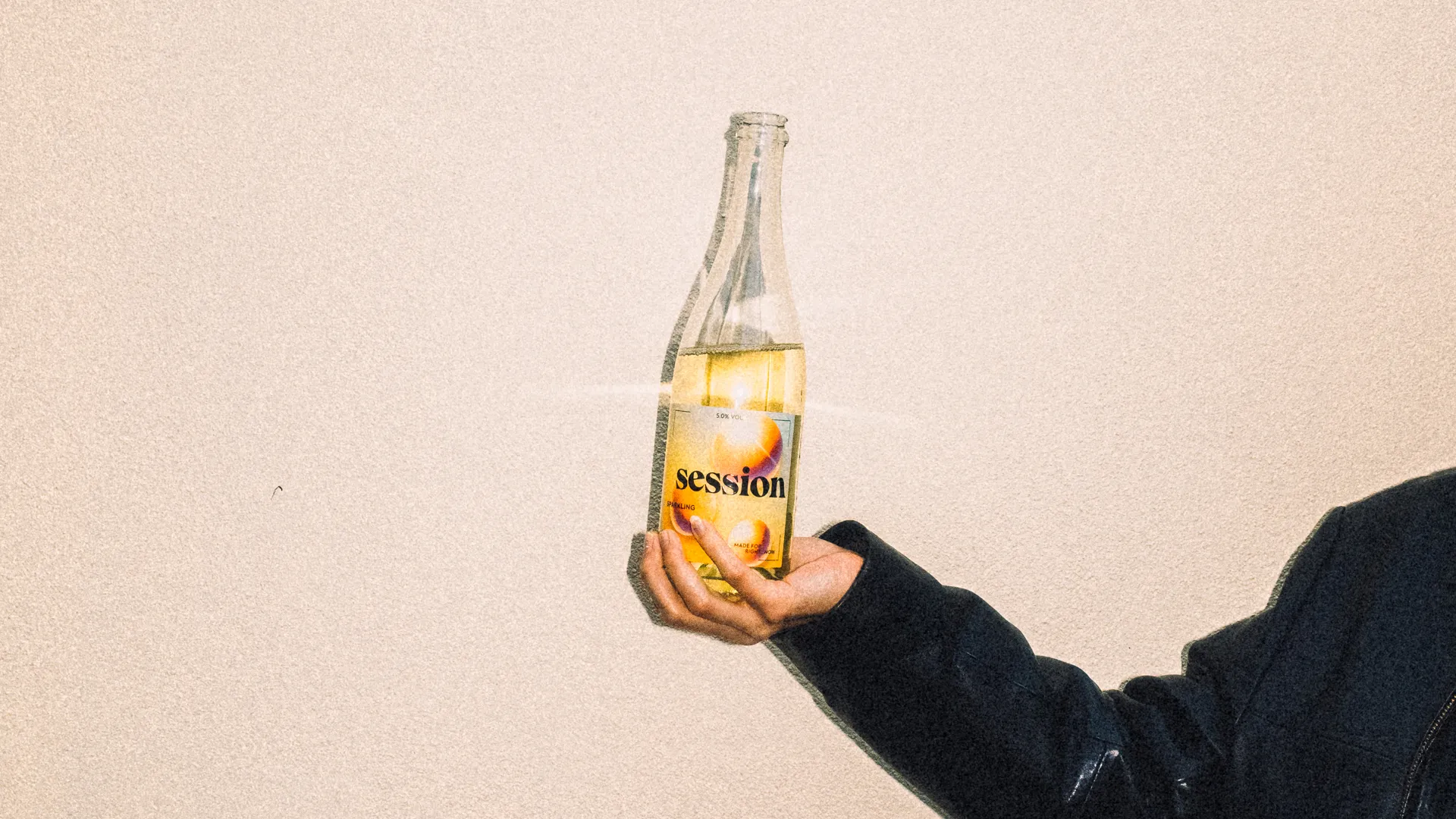SESSION WINE sparkling bottle held in sunlight with a large pale wall as background