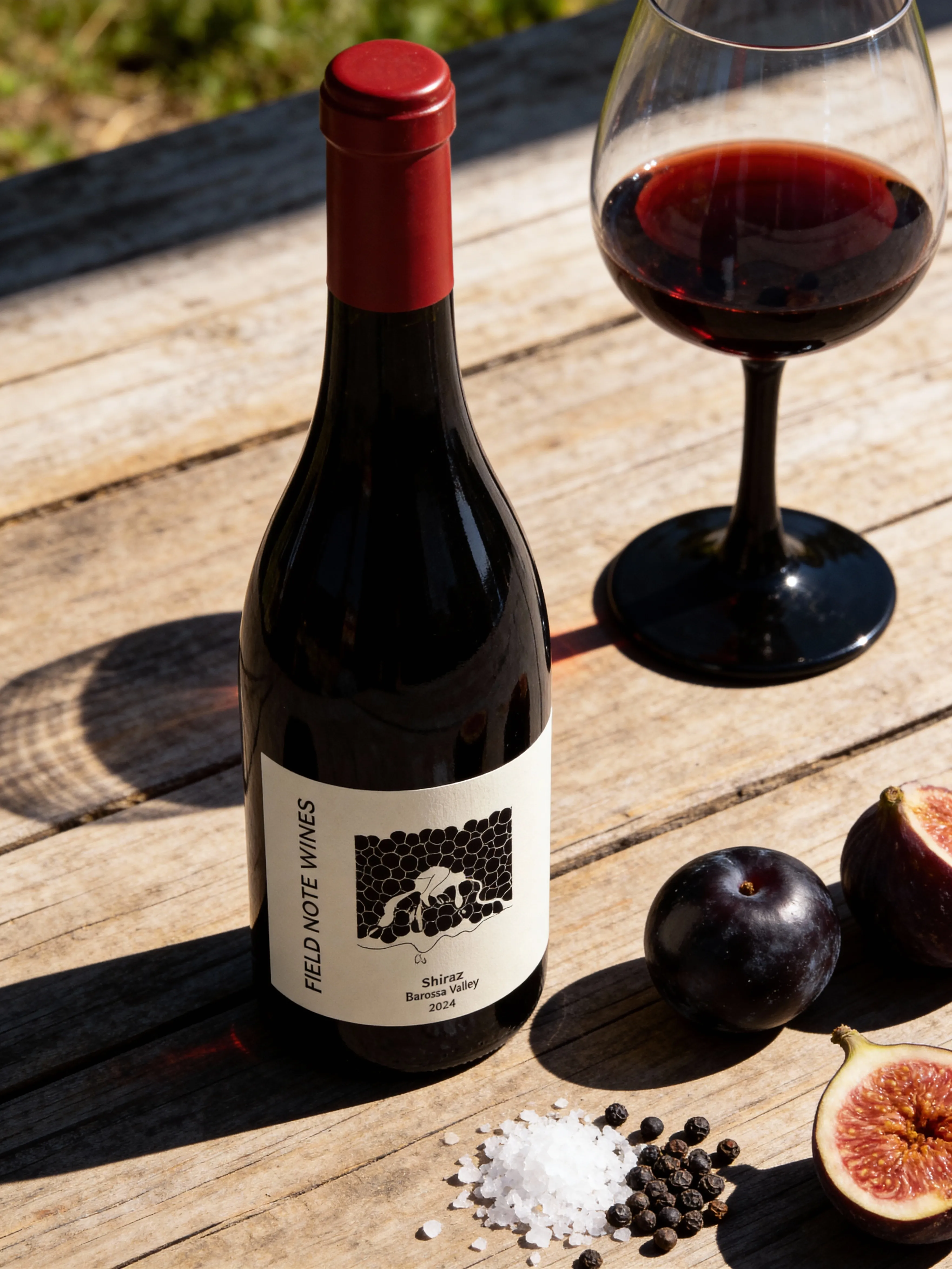 FIELD NOTE wine bottle seen close on a wooden table with fruit and peppercorns