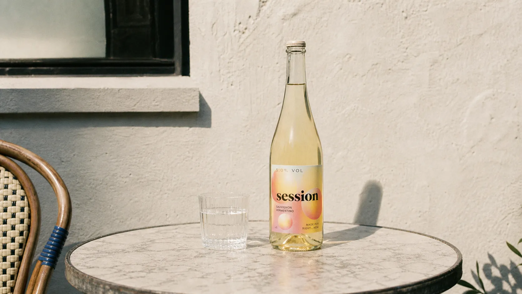 SESSION WINE bottle standing fully on a small outdoor cafe table beside a clear glass