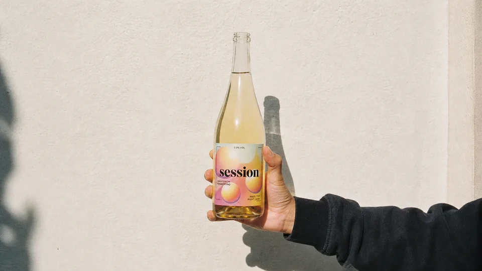 SESSION WINE bottle held against a pale wall